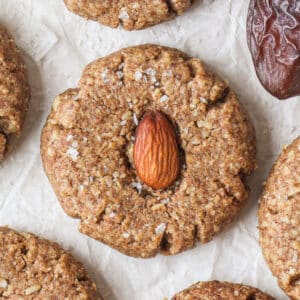 Ein mit einer Mandel dekorierter Mandelmus Cookie, mitten zwischen weiteren Mandelmus Cookies die mit Mandeln und Datteln dekoriert sind.