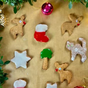 Ausgestochene vegane Weihnachtskekse mit Zuckerguss und Deko auf braunem Backpapier