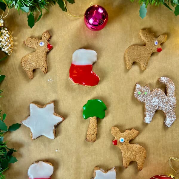 Ausgestochene vegane Weihnachtskekse mit Zuckerguss und Deko auf braunem Backpapier