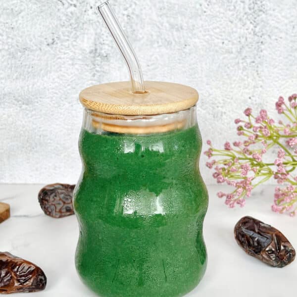 Grüner Spirulina Smoothie mit Banane, Mango und Dattel in einem Glas mit Trinkhalm